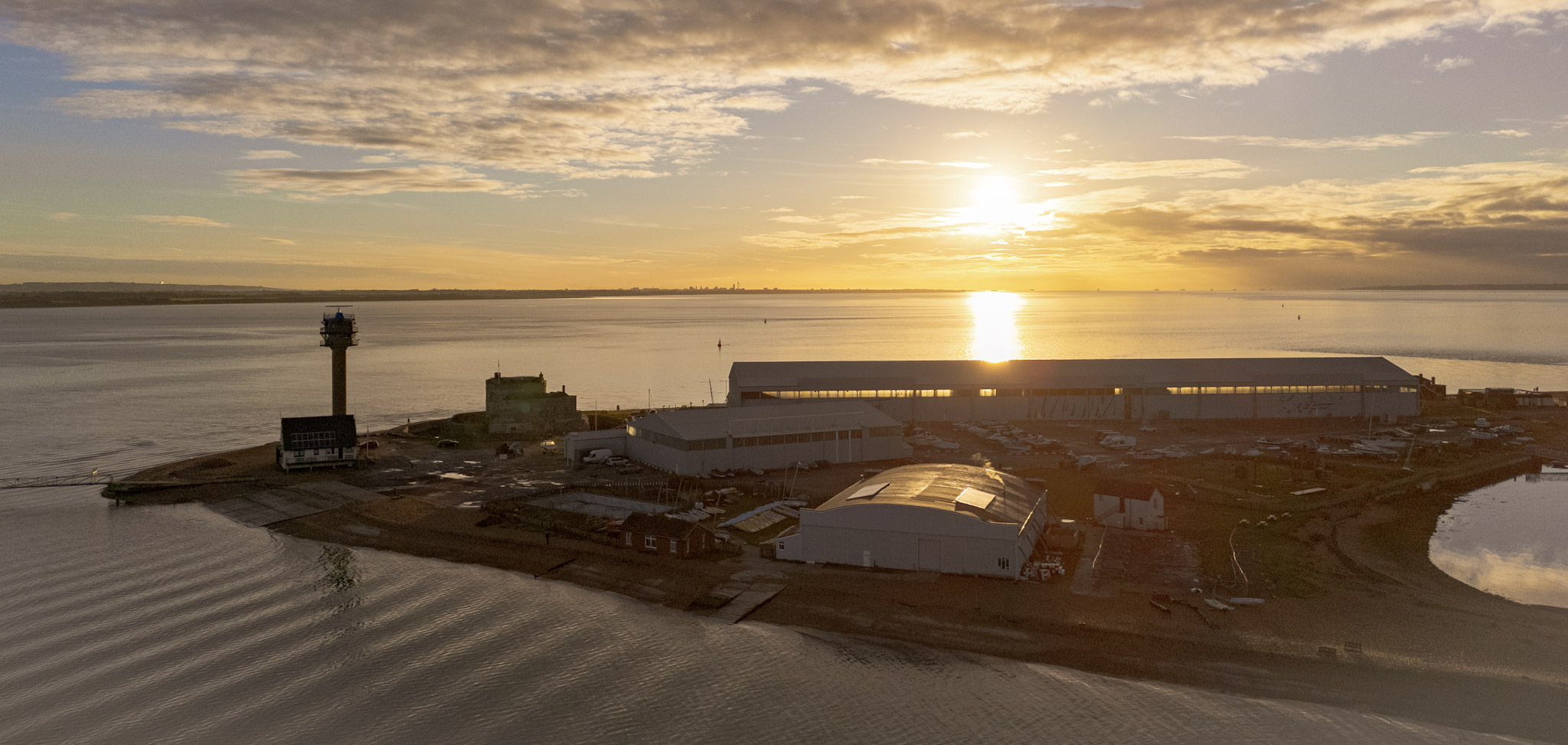 Calshot Spit, Hampshire, UK at sunrise with a yellow sky, showing the spit, the coastguard tower, the hangars and the castle