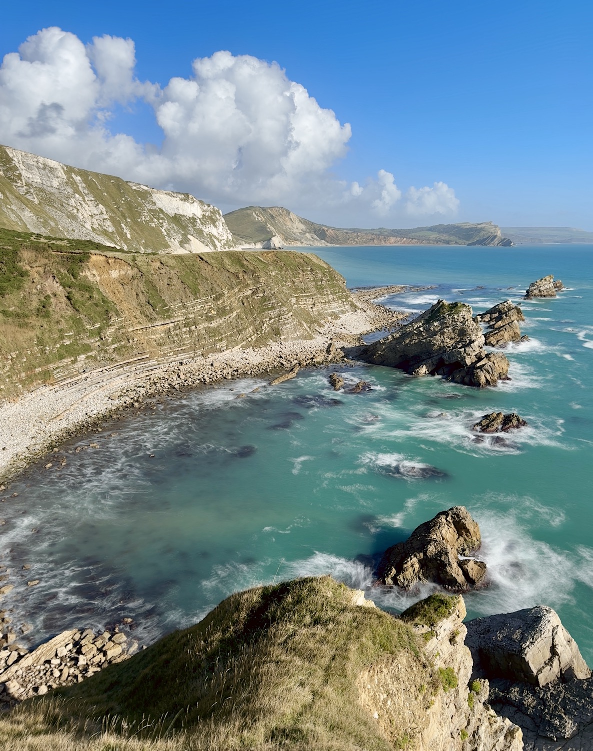 Mupe Rocks, Dorset, on a sunny day with cumulus crowds in distance and mdoerate waves crashing around the base of the rocks