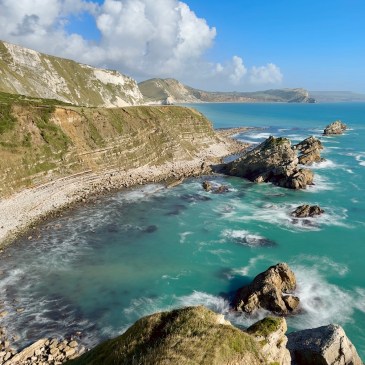 Mupe Rocks, Dorset, on a sunny day with cumulus crowds in distance and mdoerate waves crashing around the base of the rocks